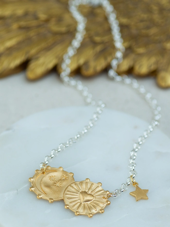 A modern celestial statement, the Lunar Glow Double Coin Necklace pairs two tactile coins in sterling silver and gold plate with a mixed metal belcher chain and star charm. Featuring sunburst and moon motifs with heartfelt engraving, this double coin necklace blends texture, symbolism and effortless style — perfect worn solo or layered.