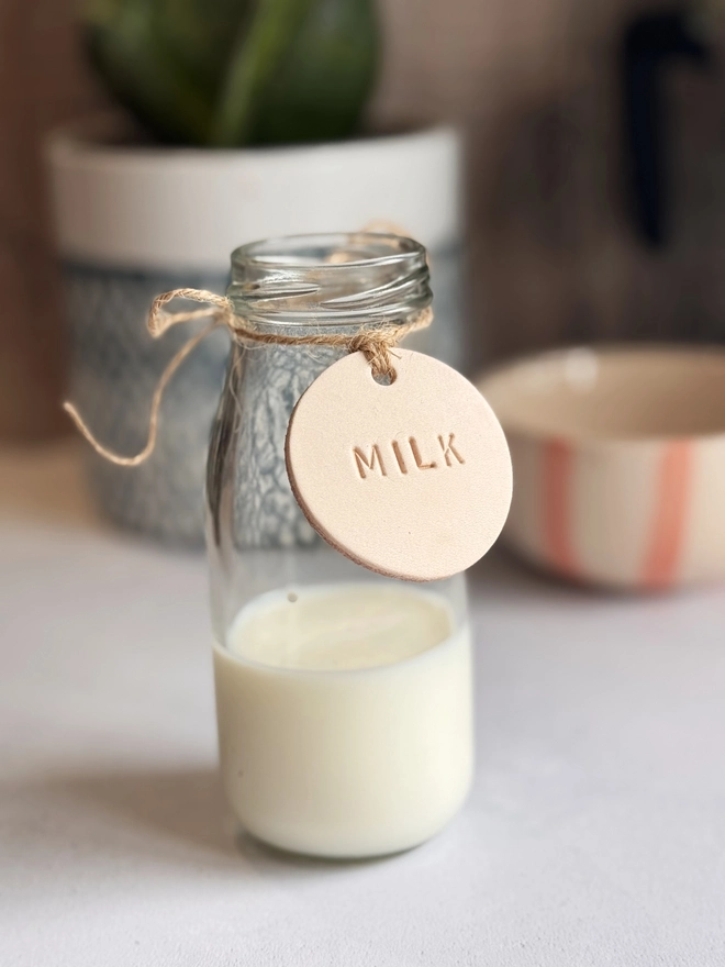 Handmade round leather label with "MILK" embossed, attached to a glass bottle with jute string. Ideal for rustic kitchen styling, pantry storage, or customisable home organisation