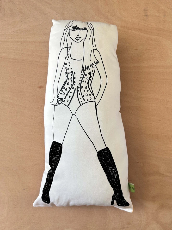 Illustrated black and white screen printed cushion of singer Taylor Swift on a light wooden surface.