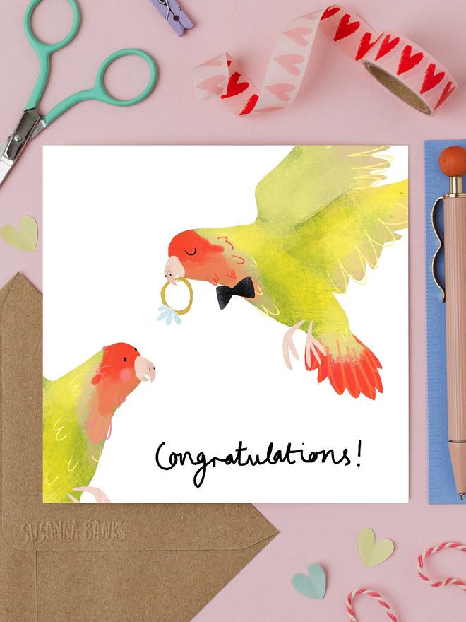 'lovebirds' illustrated engagement card. card photographed on table with assorted crafting items.