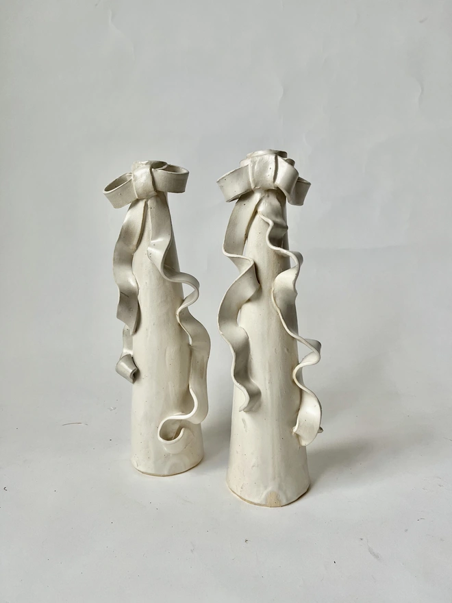 tall stoneware candlestick holder with a bow with long ribbons flowing down the candleholder 