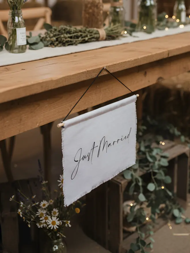 A Just Married linen hanging banner for weddings. Hanging from a rustic top table in a barn. Made from an Italian linen cotton.