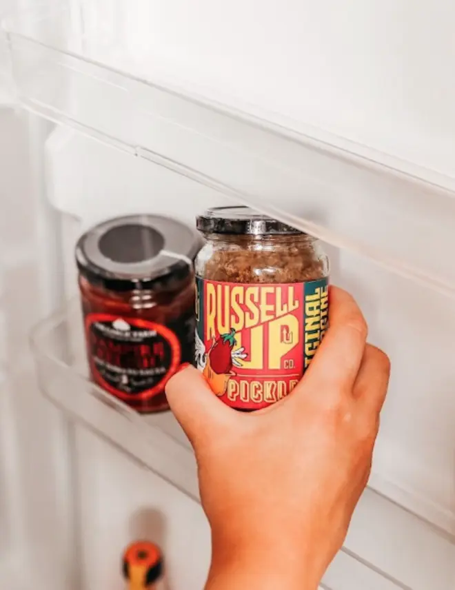 Hand holding a jar of the original aubergine pickle inside a white fridge