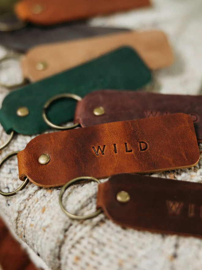 encouraging leather keyring. brown keyrings laid atop a blanket, embossed with the word 'wild'.