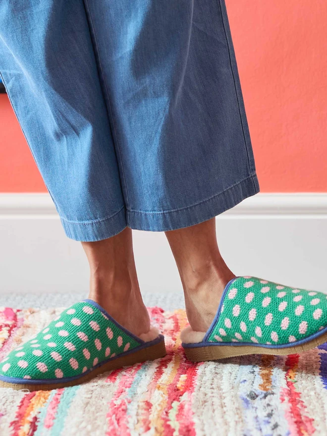 Lambswool & Sheepskin Slippers, a pair of colourful lambswool and sheepskin slippers sitting modelled in front of a colourful wall. 