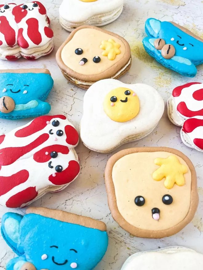 macarons decorated to look like breakfast foods (toast, bacon, fried egg & coffee cup) are arranged on a table