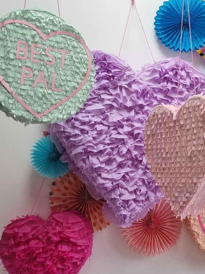 a group of heart and love heart pinatas in pastel shades with a pop of pink