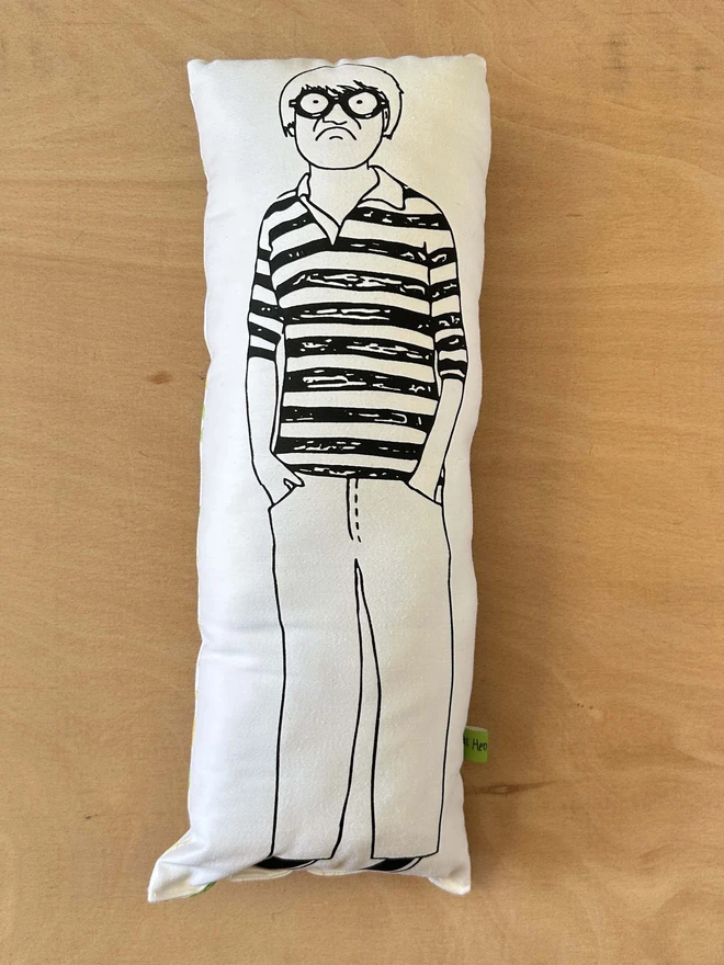 Black and white illustrated screen printed cushion of British artist David Hockney. The cushion sits on a light wood surface.