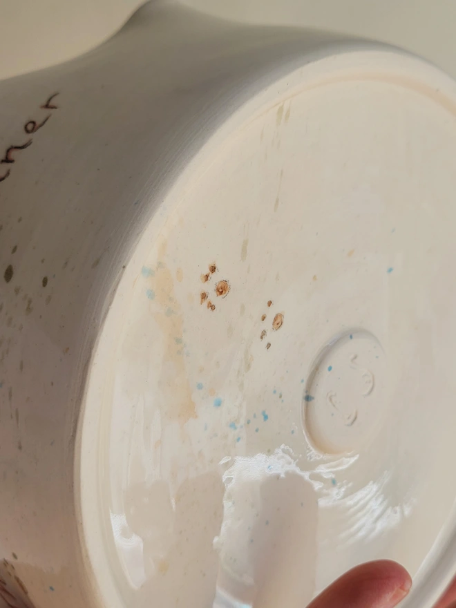 ivory ceramic dog bowl with brown green and blue splatters and pawprints held in a hand