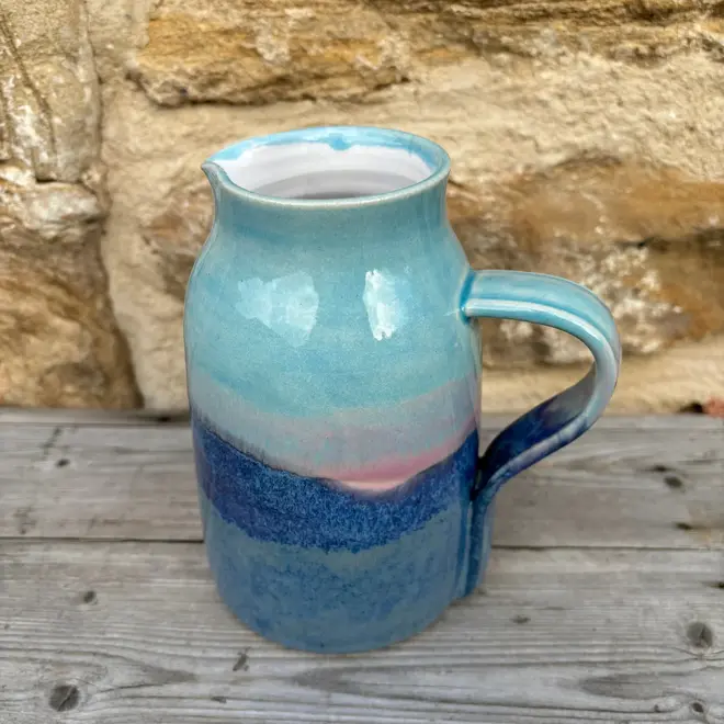 Landscape Medium Jug, a colourful jug sitting on a wooden surface against a brick backdrop. 
