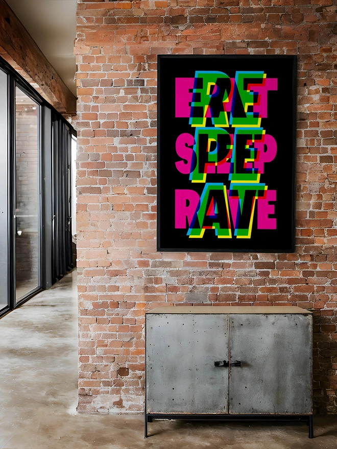 A colourful neon typographic giclée poster with the words "Eat Sleep Rave Repeat" hangs on a brick factory apartment. An ideal gift for an old raver!