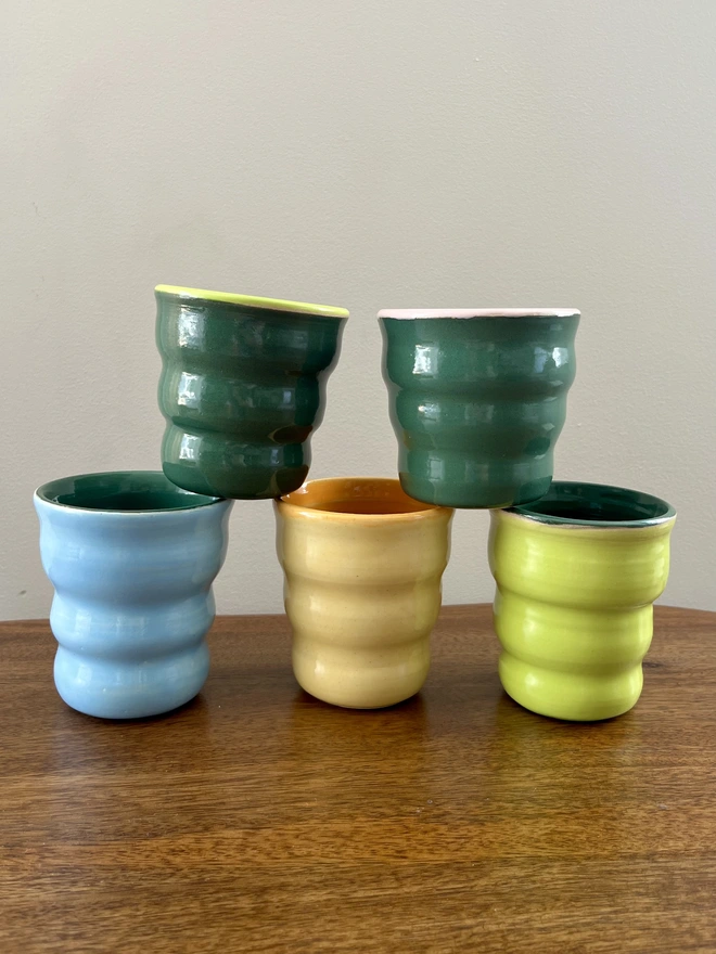 a stack of colourful ceramic tumblers on a wooden coffee table