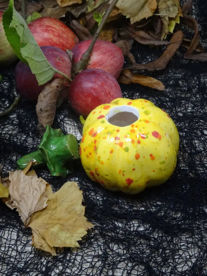 A ceramic decorative pumpkin in yellow spotted glaze with a green stem