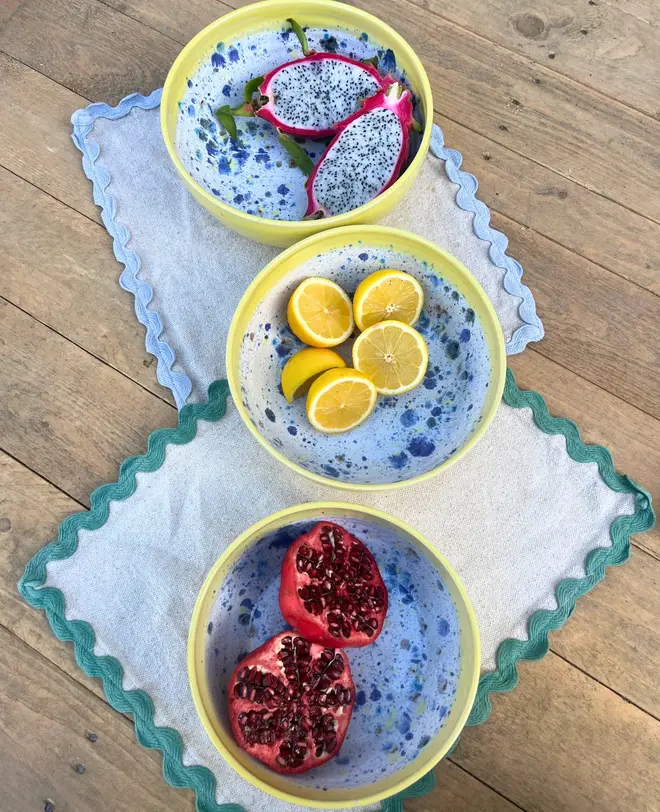 Shoreline Serving Bowls (Set Of 3), a collection of colourful serving bowls on napkins on a wooden surface. They are accompanied by fruits. 