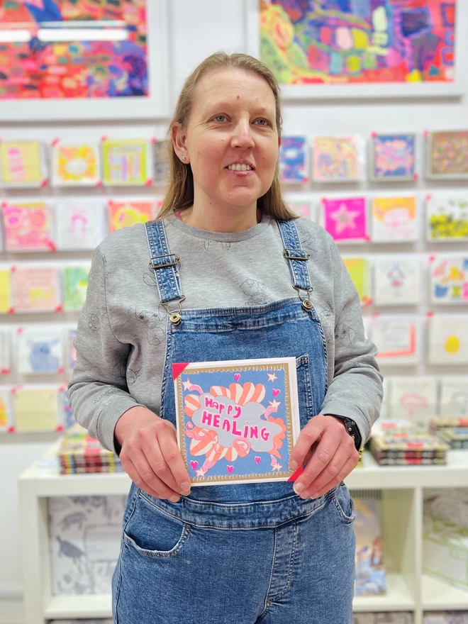 Artist holding A Positive Happy Healing card, riso printed with a pink & blue get well soon message