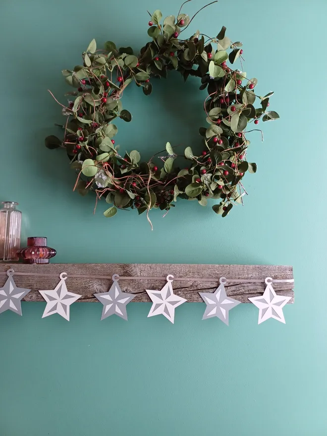 Silver and White Star Garland on Mantelpiece With Christmas Wreath Hung On Wall Above