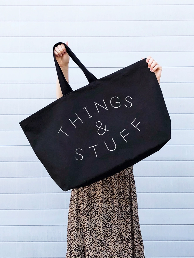 model holding up an oversized black canvas tote bag with things and stuff slogan