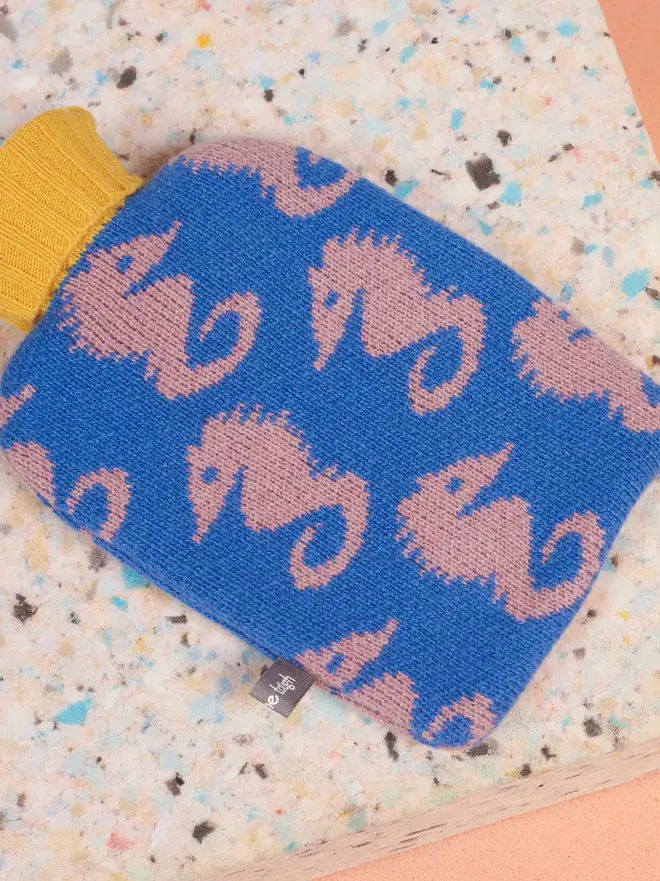 Mini Lambswool Hot Water Bottle Cover, a mini hot water bottle sitting on a colourful surface. 