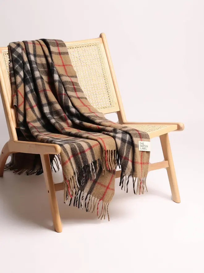 Camel Thompson Recycled Wool Blanket, a brown blanket draped over a wooden chair on a white surface against a plain backdrop. 