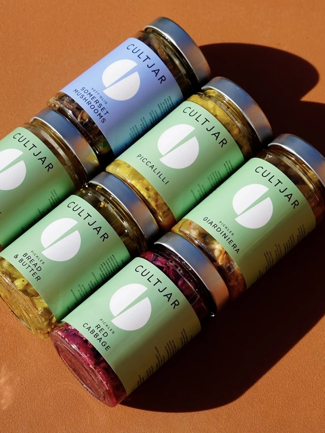 Premium Pickle Gift Pack (Set Of 6), a group of six pickle jars sitting on an orange surface. 