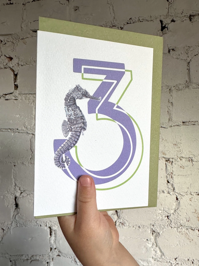 a white card with a big purple number 3 and an illustrated seahorse with a green envelope