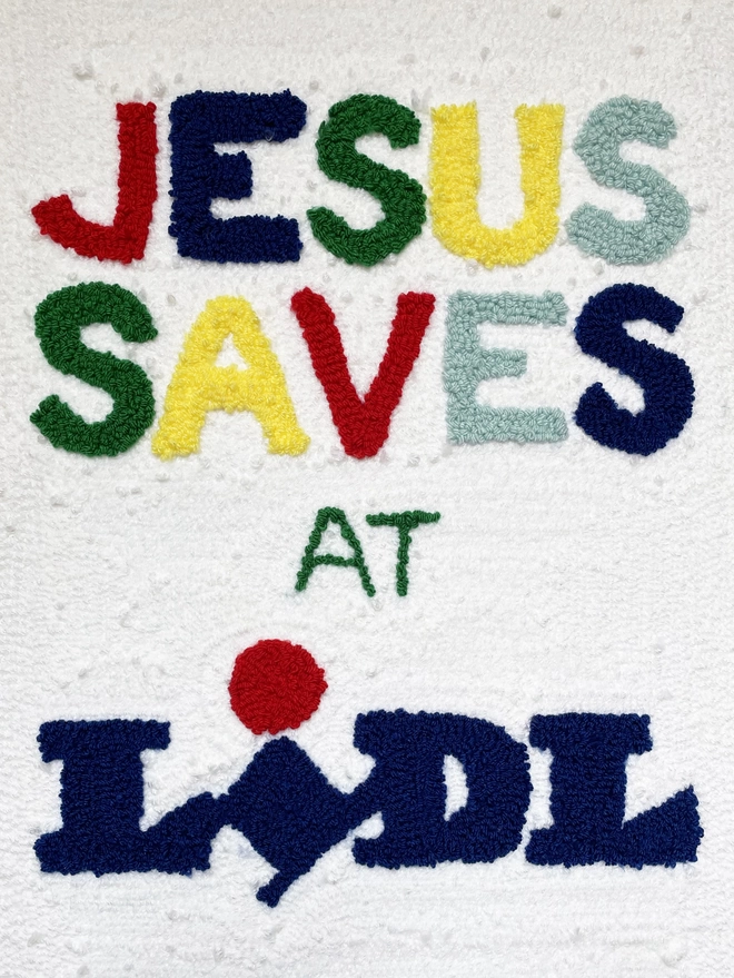 textile artwork with Jesus saves at Lidl written on a white background in bright coloured wool