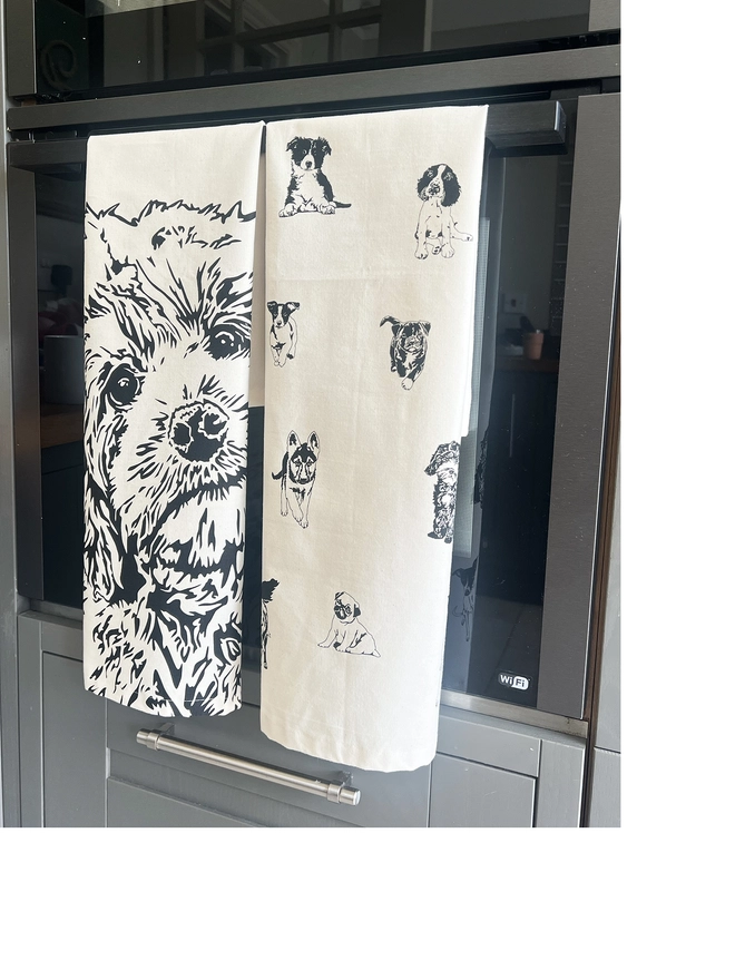 folded cockapoo tea towel next to a multi dog tea towel hanging on an oven door