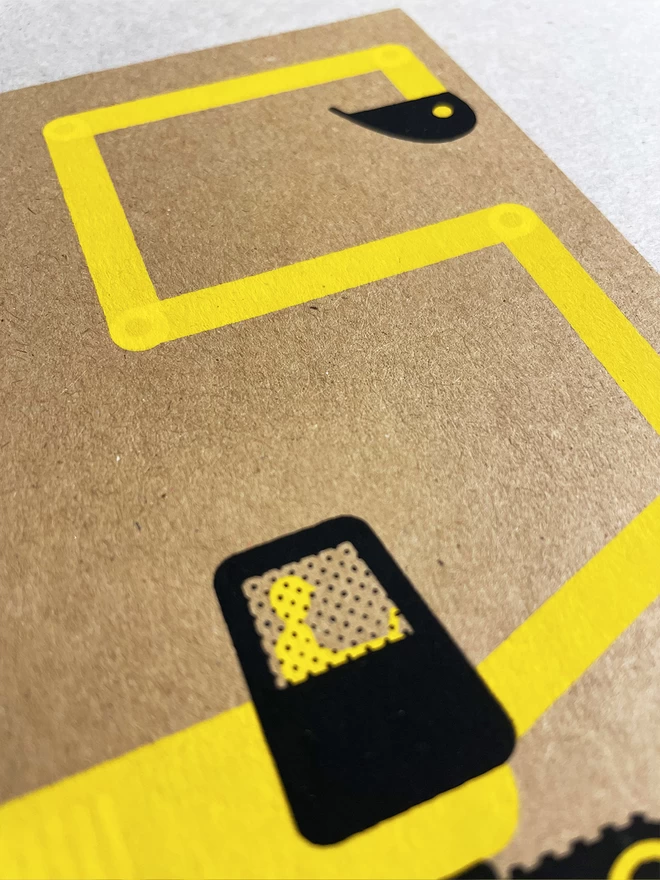 Close up of a yellow and black digger, its arm makes a number 5, screenprinted on a Kraft brown card. Stood on a white background with a light grey shadow