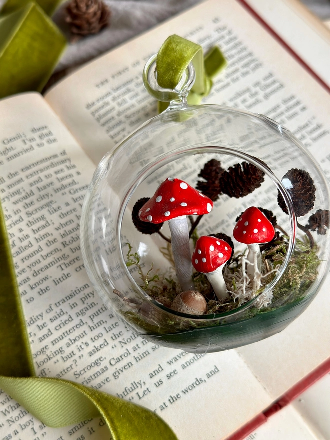 Glass Bauble filled with handmade toadstools and alder cones sitting on a vintage book 