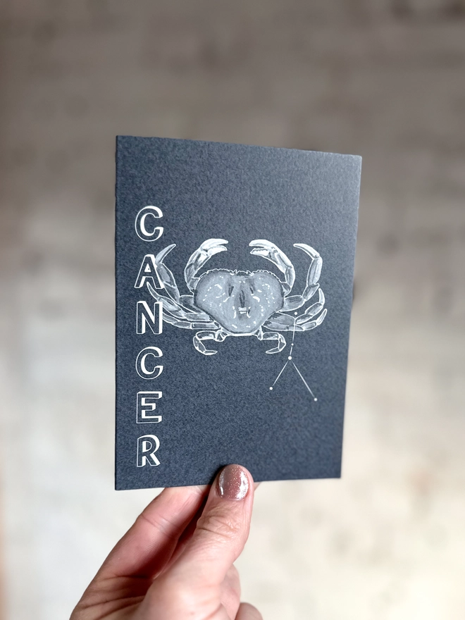 a greetings card featuring a greyscale illustration of a zodiac style crab with the text “CANCER”