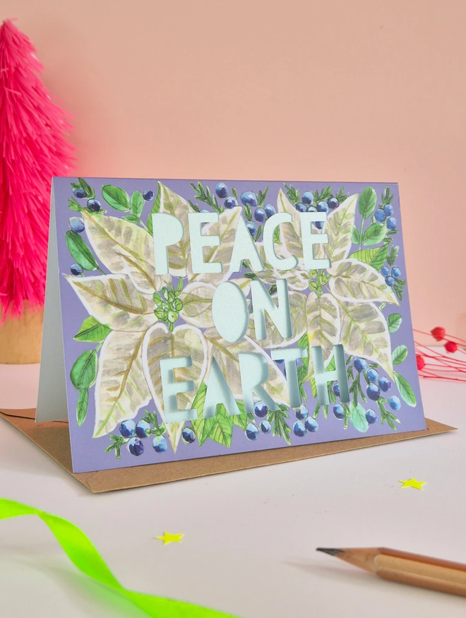 White Poinsettia Christmas Card with Peace on Earth in paper cut text and shimmering pearlescent blue blue liner 