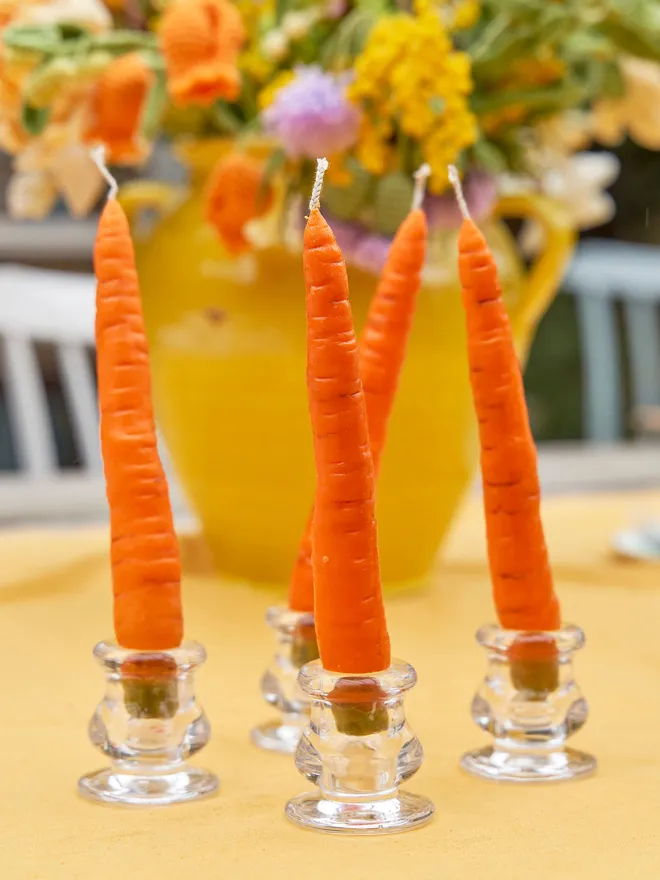 4 Fallow dinner Carrot candles held in glass candle holders, placed on a mustard tablecloth 