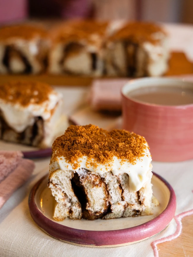 Buns of Joy Biscoff Cheesecake Buns on a plate with a cup of tea in the background