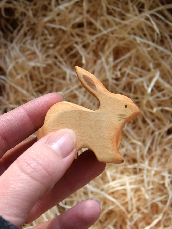 wooden toy natural rabbit held in hand above woodwool