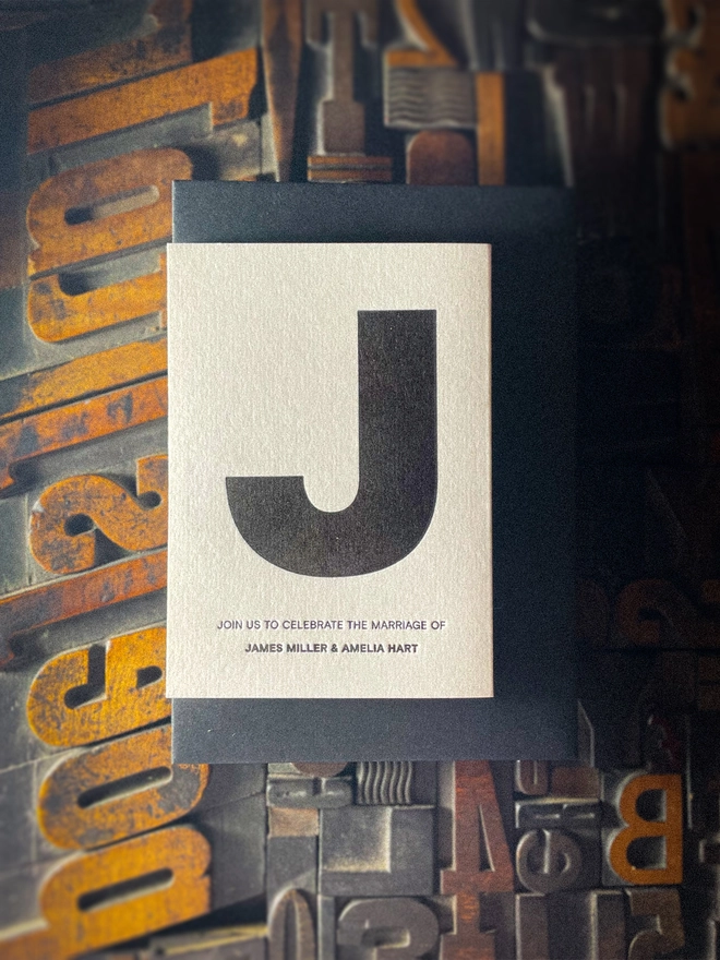 Contemporary Amour Mono wedding invitation featuring bold black initial typography on Pristine White card, paired with a contrasting black envelope.