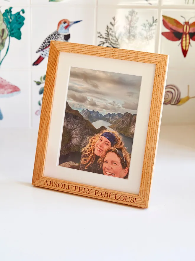 Personalised oak frame with 'Absolutely Fabulous' engraved against bird tiles and a white surface