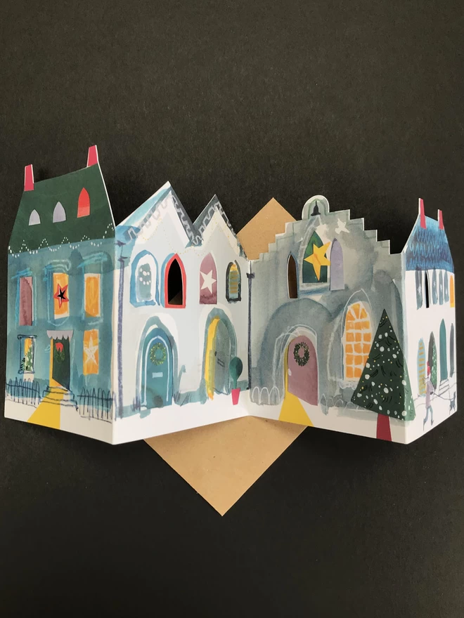 Illustrated cut-out card showing festive house with lit-up windows, rests n dark background.