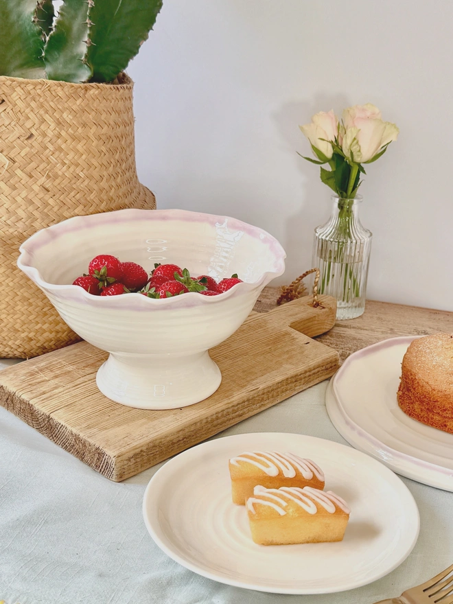 Undulating hand thrown porcelain stem bowls with satin cream glaze and pink or turquoise rim on a rustic table top