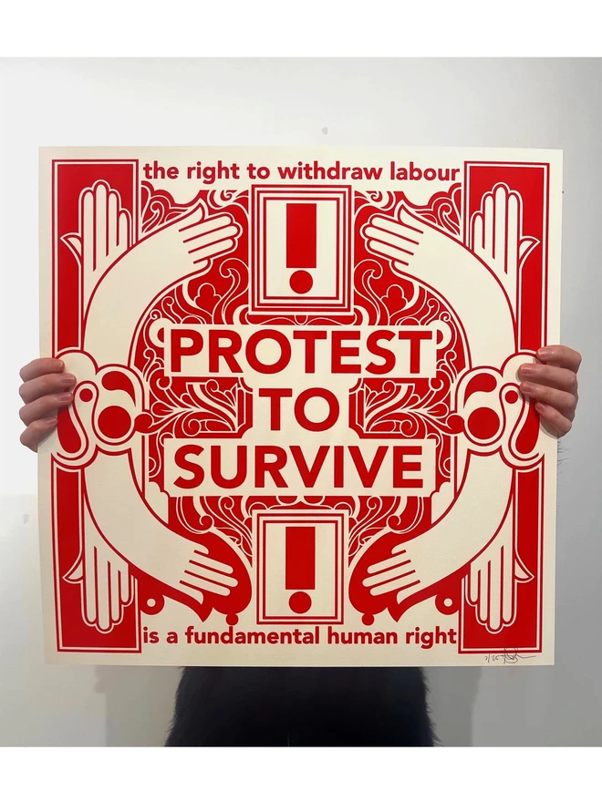 The large, bold red and white print is held in front of a person’s face, with only their fingers visible. The print says “Protest to survive” at the centre, as well as “the right to withdraw labour” at the top, and “is a fundamental human right” at the bottom. 