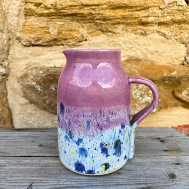 Shoreline Medium Jug, a colourful jug sitting on a wooden surface against a brick wall backdrop. 