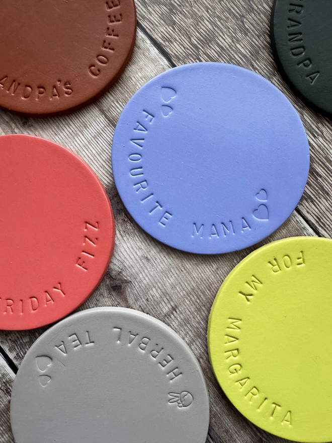 Handmade leather coasters in various colours, embossed with personalised messages like 'Herbal Tea' and 'Favourite Mama.' Stylish and durable drink coasters, perfect for gifts and home decor.