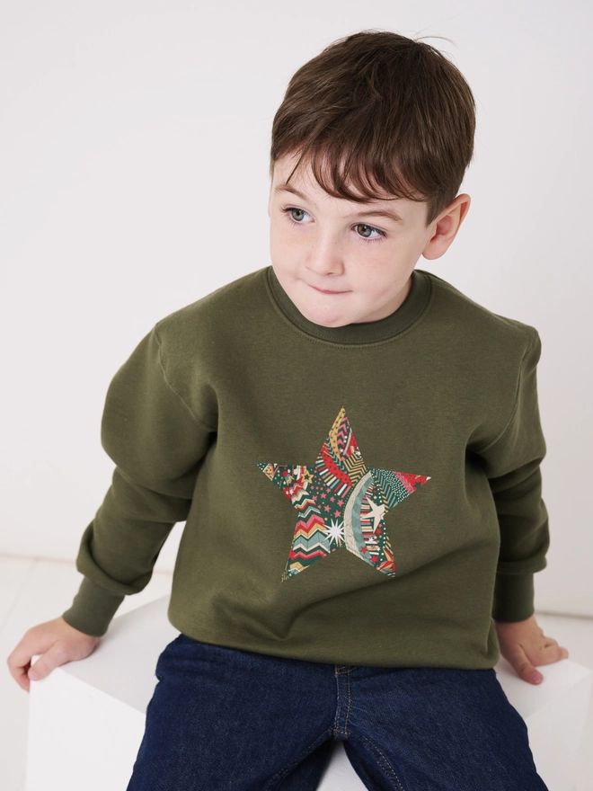 a 5 year old boy wearing a khaki christmas sweatshirt with a festive liberty print star on the front 