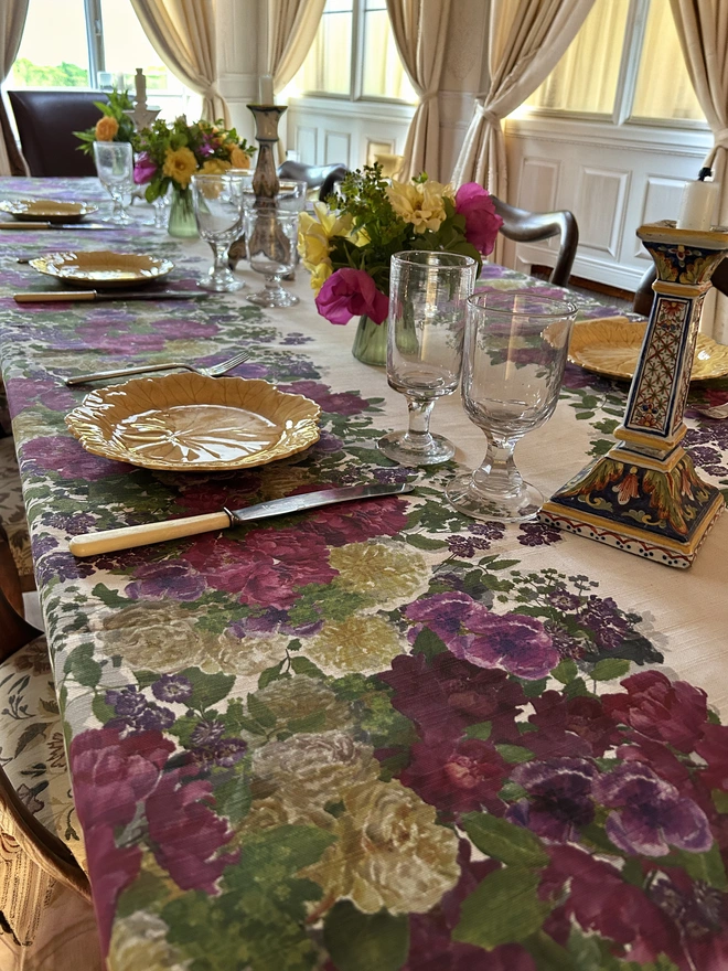 A celebration table decorated with glassware and a white linen tablecloth covered in hand painted summer roses