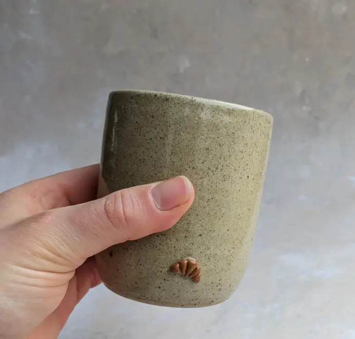 Biscuit coloured croissant coffee cup with a subtle croissant design, placed against a grey marble background.