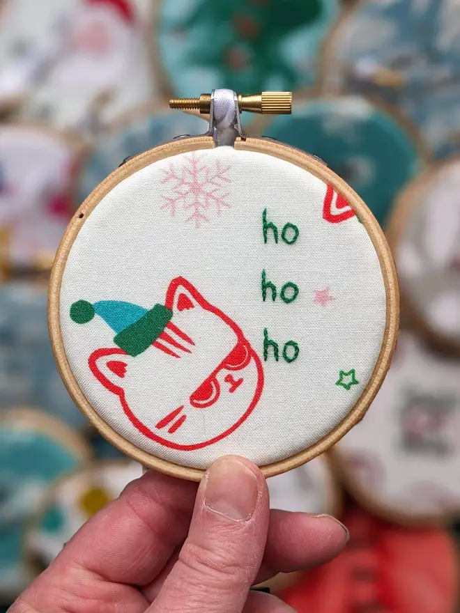 A hand embroidered hoop on Christmas fabric reading ho ho ho