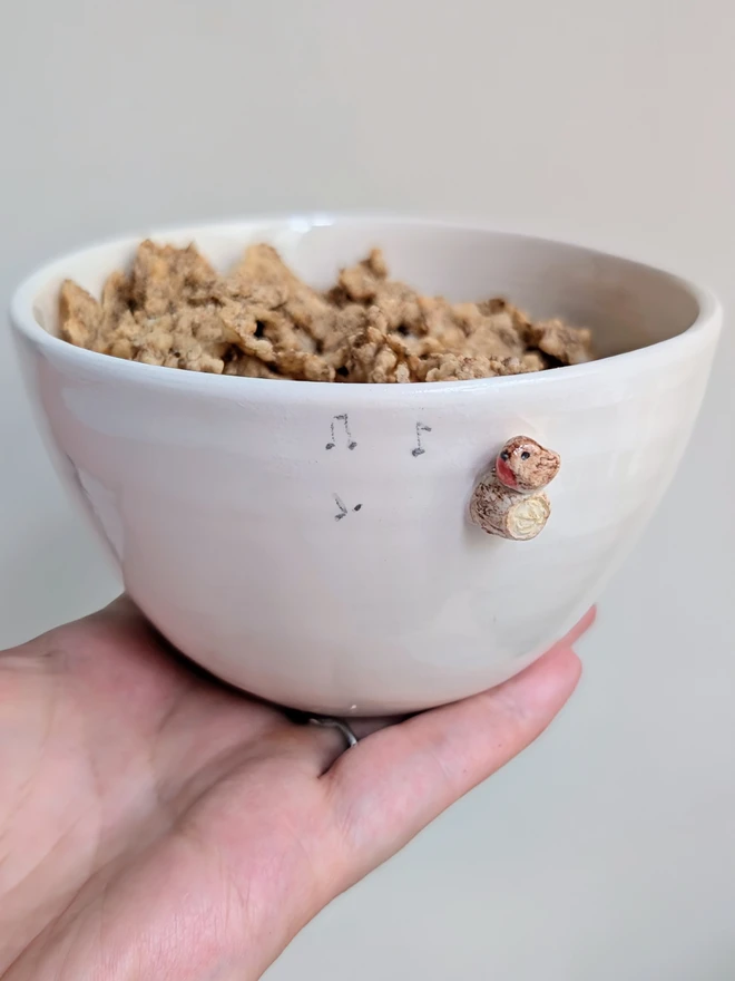 white ceramic bowl with a tiny modelled robin perching on a modelled branch with musical notes