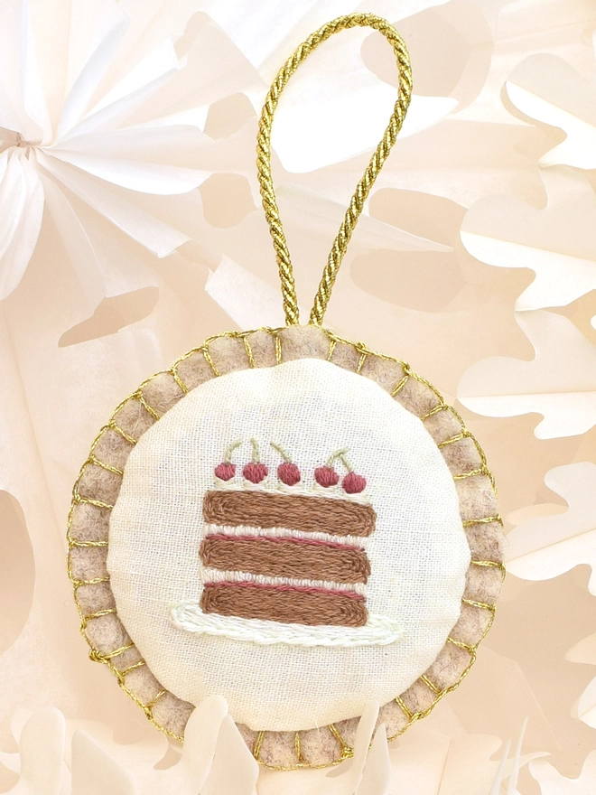 The finished Gateau embroidery turned into a felt bauble, displayed amongst paper-cut stars.