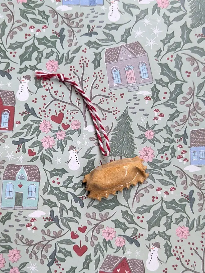 ceramic agnolotti christmas decoration. a small ceramic pasta decoration hanging from red and white thread.