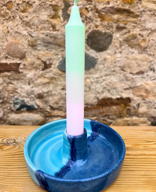 Landscape Candle Stick Holder, a colourful candle stick holder accompanied by a candle sitting on a wooden surface against a brick backdrop. 