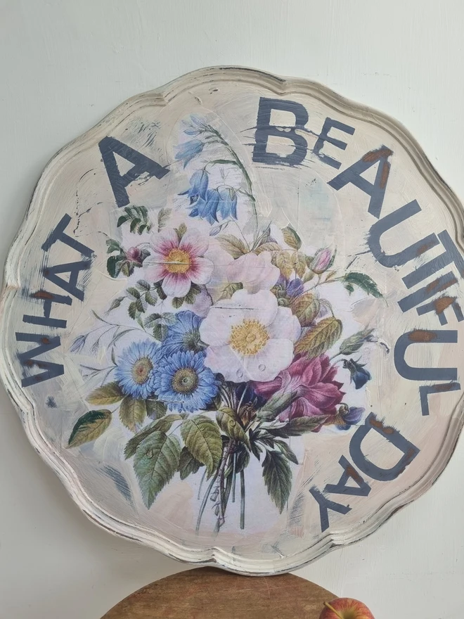 Art Panel made from a 'pie crust' table top. A pale background with mauve flowers and writing in mauve that says 'what a beautiful day'.